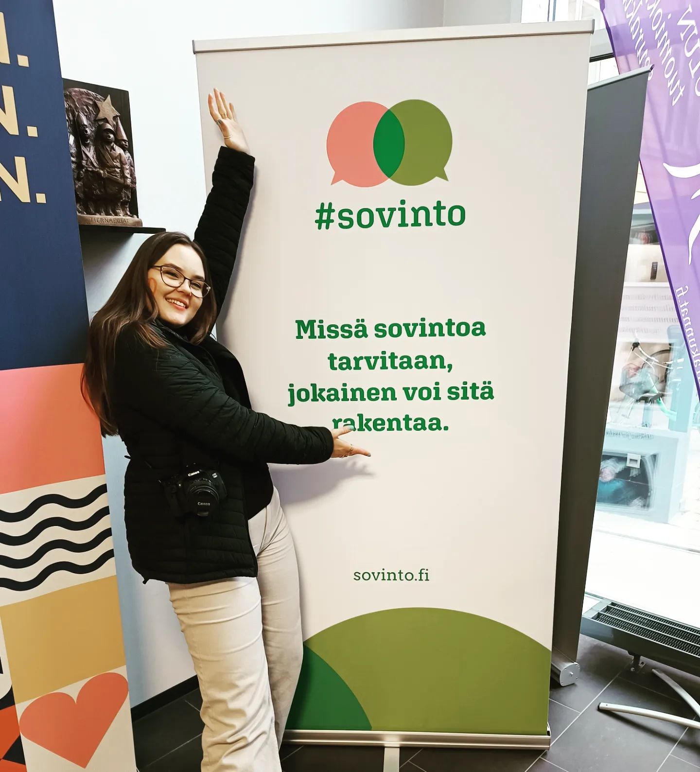 Nuori nainen esittelee #sovinto-aiheista julistetta, jossa on teksti "Missä sovintoa tarvitaan, jokainen voi sitä rakentaa.