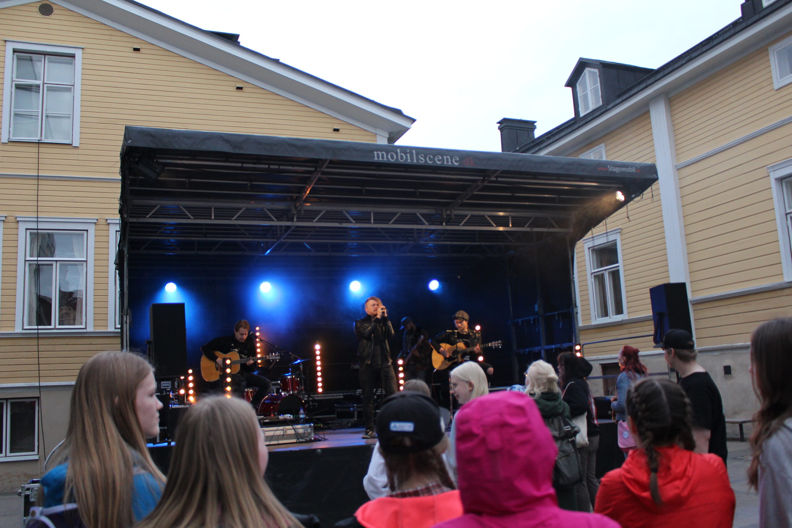 Lavalla esiintyy bändi, ja yleisö seuraa esitystä iltahämärässä.