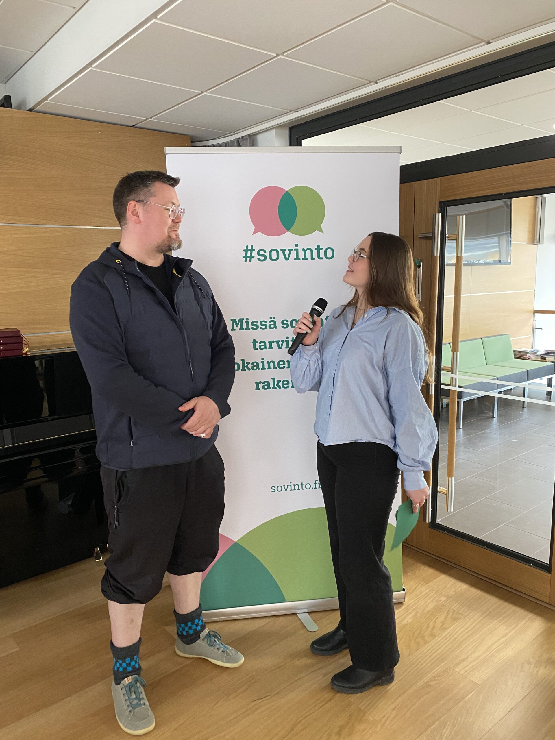 Kuvassa nuori nainen haastattelee miestä, taustalla on #sovinto-teemainen banneri.