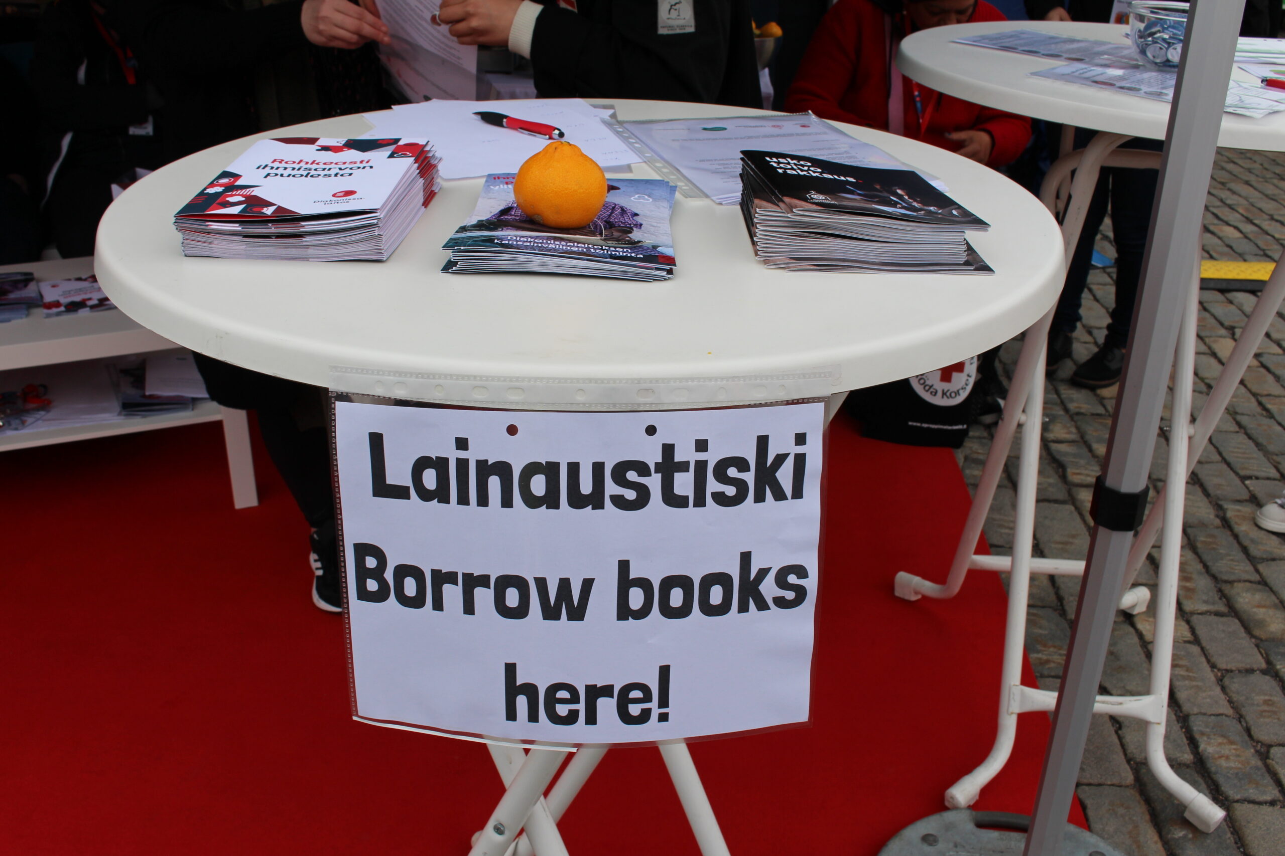 Pöydällä on lainauspiste, jossa on kirjoja ja opaste "Lainaustiski" sekä "Borrow books here!".